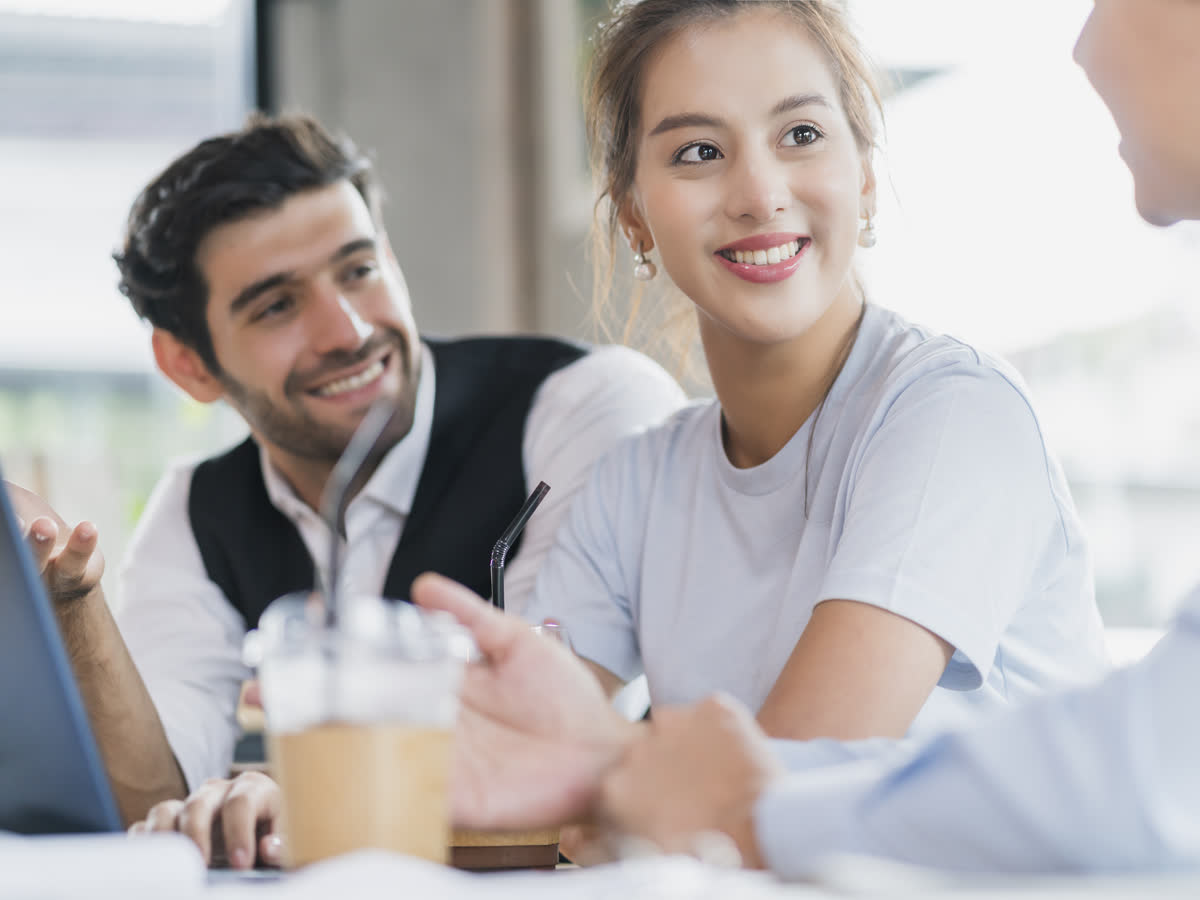 Three colleagues talk through a plan together around a laptop in a bright cafe